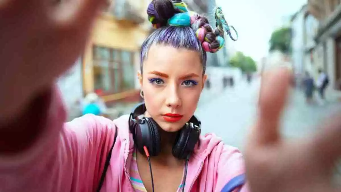 Cool funky young girl with headphones and crazy hair enjoy power of music taking selfie on street