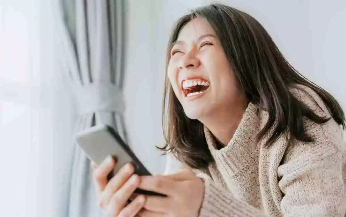 Happy Asian woman laughing while lying on the bed using smartphone mobile at home
